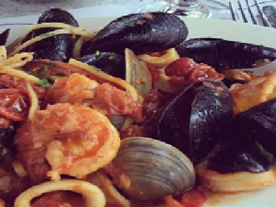 White plate of seafood pasta, basket of bread, glass of red wine