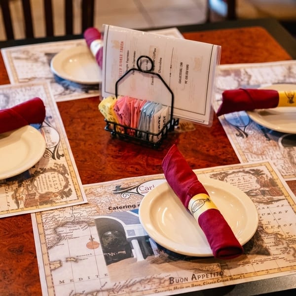 Restaurant table set with placemats, plates, red napkins, and a menu with sugar packets.