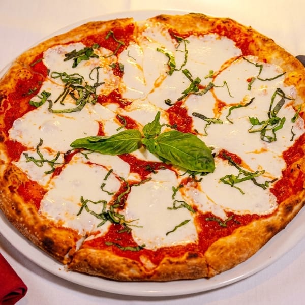 Margherita pizza with fresh basil leaves and mozzarella cheese on a white plate with a red napkin.