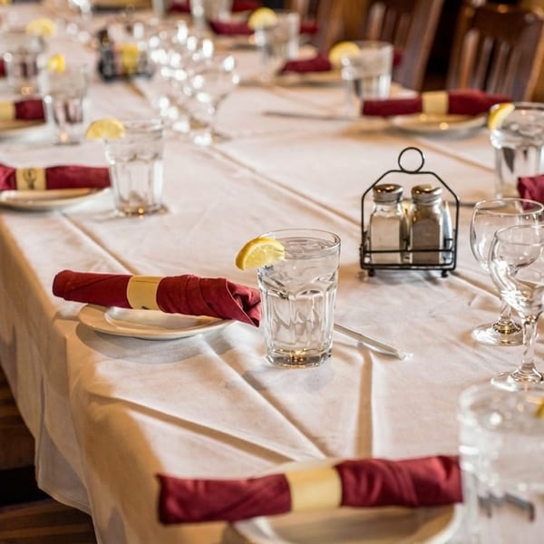 Long dining table set with white tablecloths, red napkins, water glasses with lemon, and wine glasses.