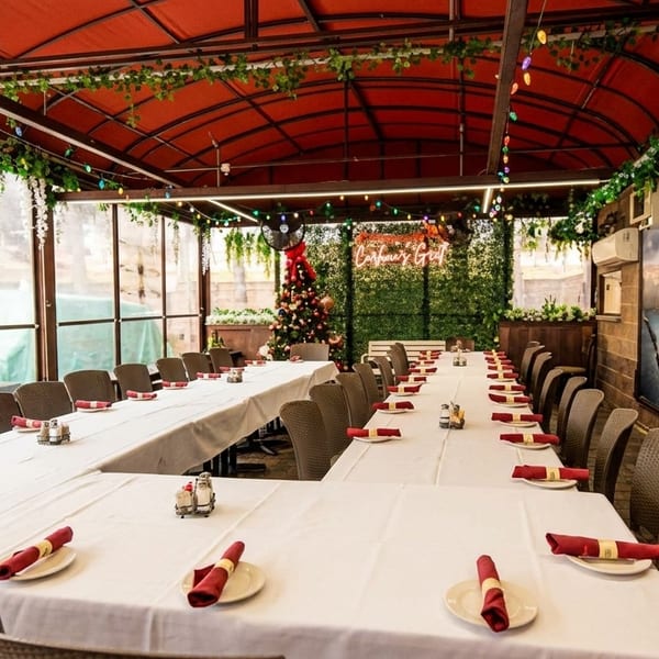 An empty restaurant patio with tables set for a large party, decorated with string lights and a mural.