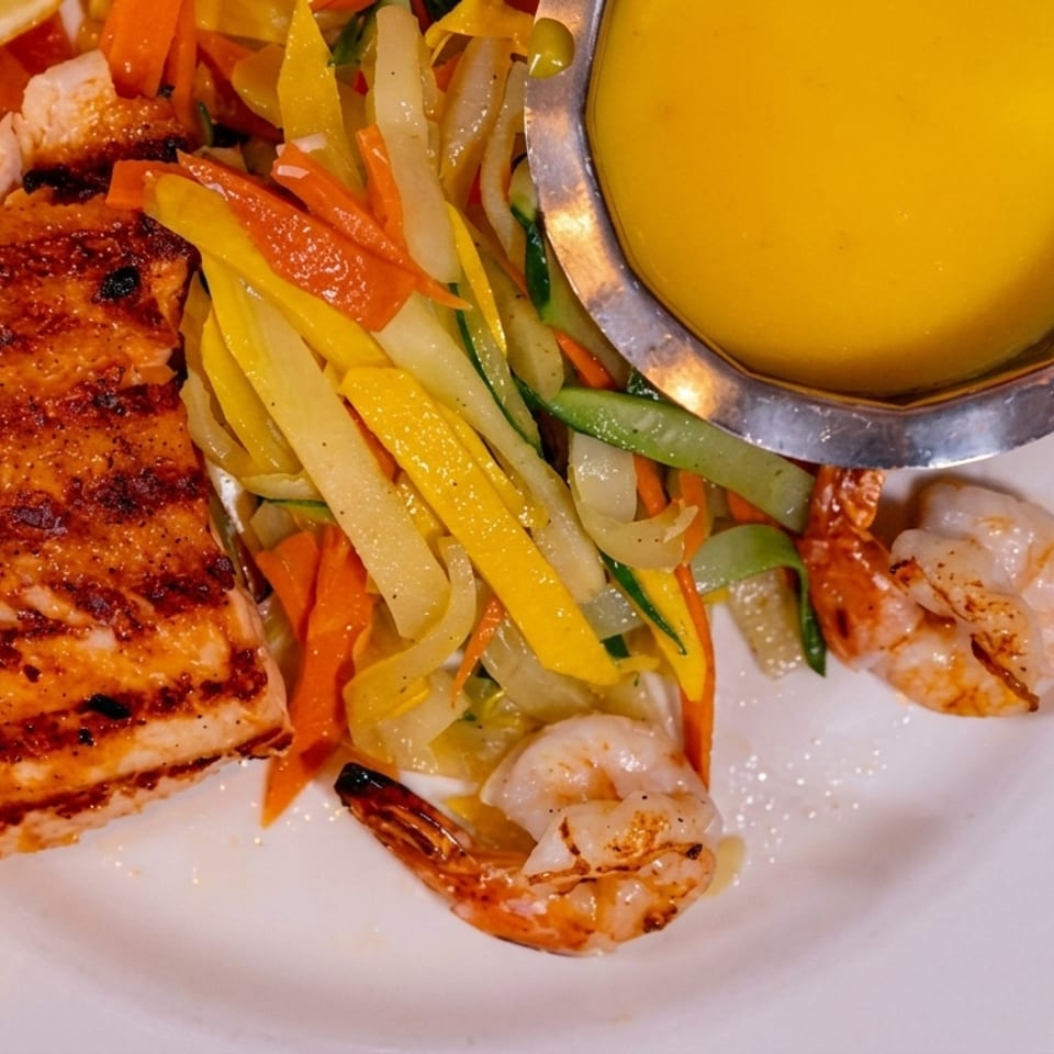 Grilled salmon and shrimp with colorful julienned vegetables and a side of yellow sauce.
