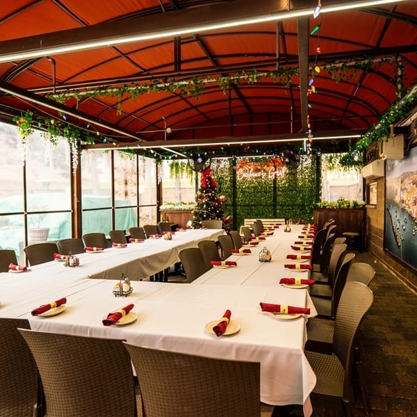 Long tables with white tablecloths and red napkins in a covered outdoor dining area with festive lights.