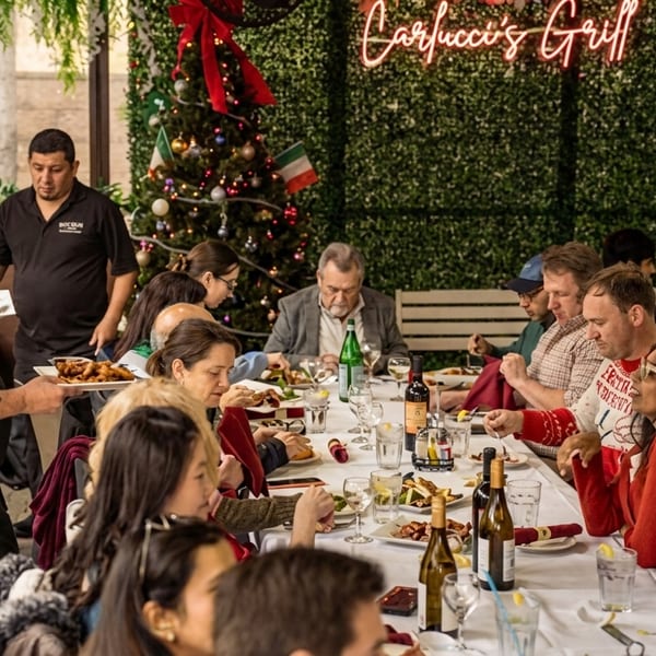 Waiters serve food to a large group of people dining at Carfucci's Grill, decorated for Christmas.