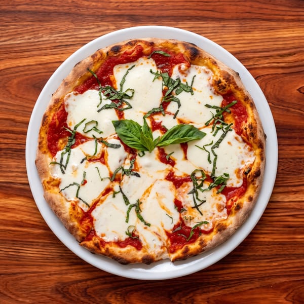 Overhead view of a Neapolitan Margherita pizza with melted mozzarella, tomato sauce, and fresh basil on a white plate.