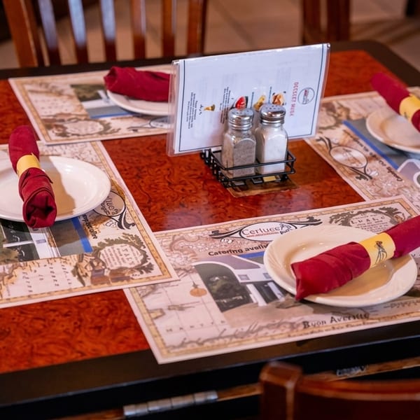 A restaurant table set with placemats, white plates, red napkins, and a menu with salt and pepper shakers.