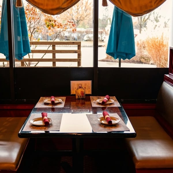 Empty restaurant booth with brown leather seats, a set table, and large windows overlooking a patio.