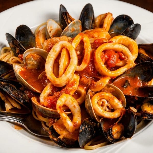 Seafood pasta with mussels, clams, calamari, and shrimp in red sauce on a white plate.