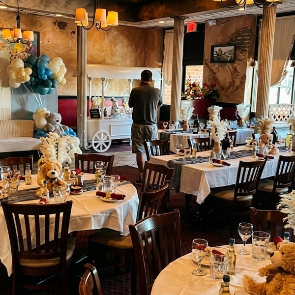 Restaurant dining room set for a baby shower with blue and white balloons, teddy bears, and decorated tables.