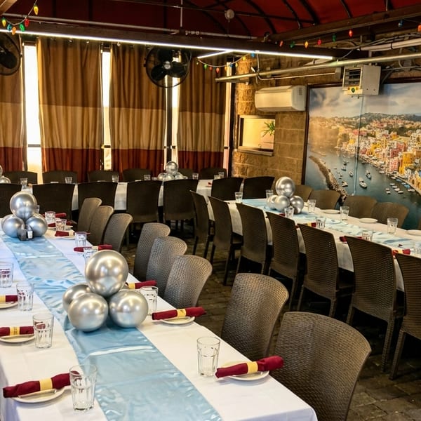 Long dining tables set with white tablecloths, blue runners, and silver balloon centerpieces in a restaurant.