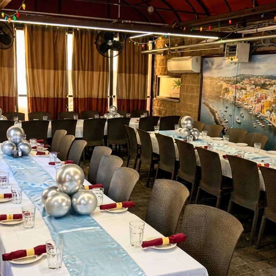Long dining tables set with white tablecloths, blue runners, and silver balloon centerpieces in a restaurant.